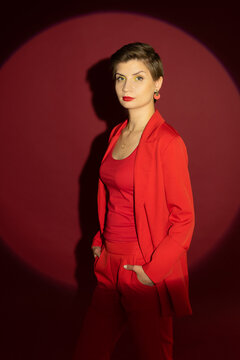 Gorgeous sexy seductive lady in a red (jacket, T-shirt. trousers), with a short haircut and bright makeup, posing in the studio on a red background in the spotlight in a circle of light