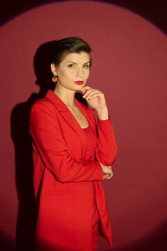 Gorgeous sexy seductive lady in a red (jacket, T-shirt. trousers), with a short haircut and bright makeup, posing in the studio on a red background in the spotlight in a circle of light