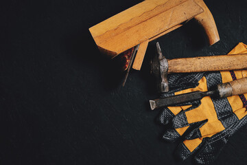 Set of tools for carpenters, hammer, chisel and plane with gloves dark wooden background.