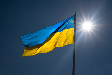 Ukrainian flag against a blue sky with a bright sun.