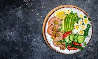 Ketogenic breakfast. Keto low carb shrimps, prawns, quail eggs, fresh salad, tomatoes, cucumbers and avocado on a dark background. keto diet. Top view
