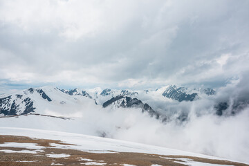 Fototapeta na wymiar Awesome aerial view to high snowy mountains in dense low clouds. Minimal landscape with beautiful mountain peaks in thick clouds. Simple minimalism with snow mountain tops in cloudy sky above clouds.