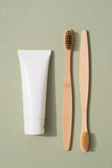Vertical image of wooden bamboo toothbrush and tube with organic mineral toothpaste on green...