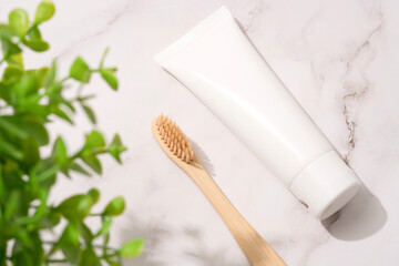 Fototapeta na wymiar Wooden bamboo toothbrush and tube with organic mineral toothpaste on white marble table background. White plastic tube with toothpaste. Eco bath products, mockup