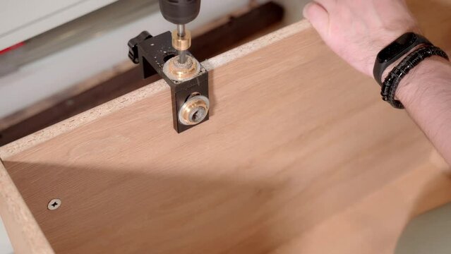 The master uses a jig template and an electric screwdriver to drill holes when assembling the cabinet.