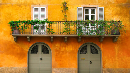 Orange Italian house facade in a typical town of Italy with green doors and balcony with white...
