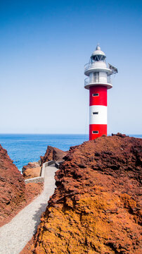 Beautiful red and white lighthouse building on volcanic shore of Tenerife Island in Spain. Atlantic Ocean background, vertical photo.