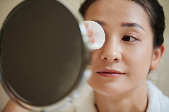 Young woman removing eye makeup with cotton pad soaked in micellar water