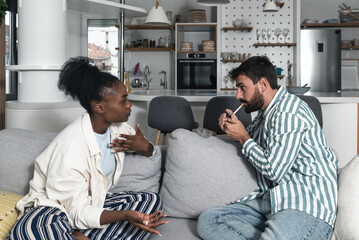 Young couple woman is unhappy while her boyfriend lighting a cigarette because she is against...