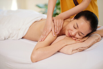 Fototapeta na wymiar Professional masseur massaging back of young Asian woman in spa salon
