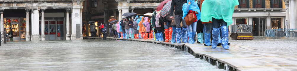 People with rainwear walking on the elevated walkway in the Square of Saint Mark in Venice in Italy...