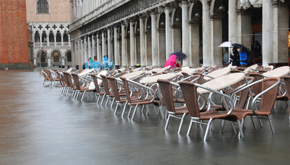tables and chairs of the alfresco bar in the flooded Square of Saint Mark during tide in Venice in...