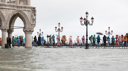 People with rain gear walking on the elevated walkway in the submerged Square of Saint Mark in...
