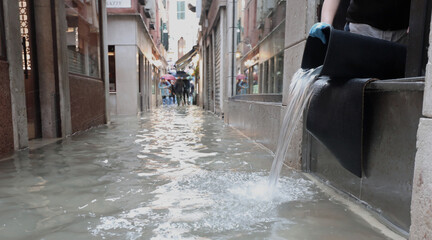 person empties the bucket of water from inside the flooded shop in the alley of Venice in Italy...