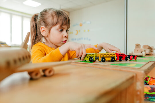 Little girl playing with wooden train on the table at kindergarten