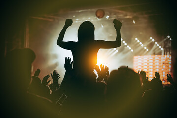 Girl silhouette with raising hands and mobile phone during enjoying music concert.