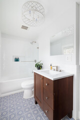 A renovated bathroom with a blue and white mosaic tile floor, wood vanity cabinet, white...