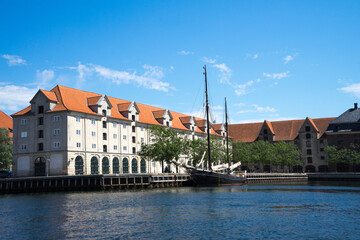 Obraz premium View of waterfront of Copenhagen, Denmark, old houses with tiled roofs and a sailing ship with lowered sails on a wooden dock on a sunny summer day