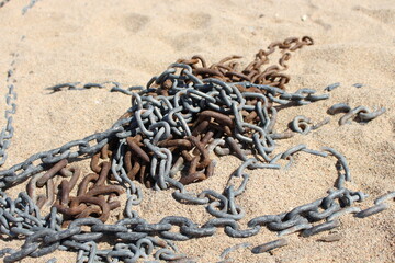 Different silver and brown chains, a little rusty, lie on the ground on the sand of a beautiful...