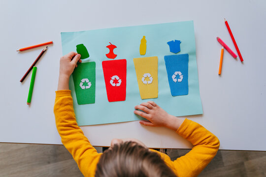 Little girl playing with poster of garbage containers for sorting at kindergarten