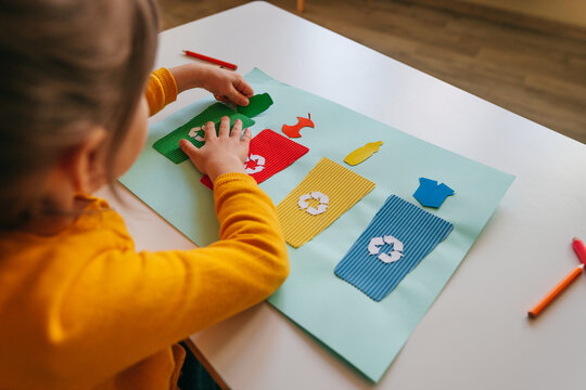 Little girl playing with poster of garbage containers for sorting at kindergarten