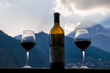 Georgian red wine with a panoramic evening on Mount Kazbegi in the Greater Caucasus Mountains in Georgia. Clouds are covering the snow-capped summit. Sunset, sunrise. Romantic date, two wine glasses.