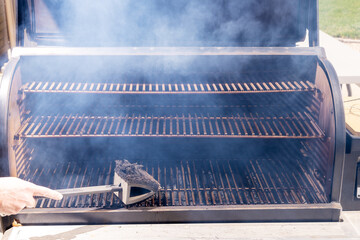 Pitmaster uses a brush to clean grill of a smoker
