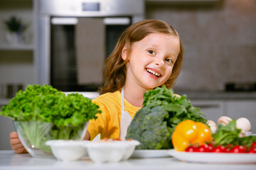 A happy child looks out from behind fresh greens and vegetables.