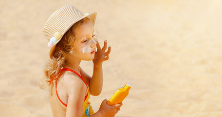 The child holds a bottle of moisturizing Sunscreen in his hands and puts a protective layer on his...