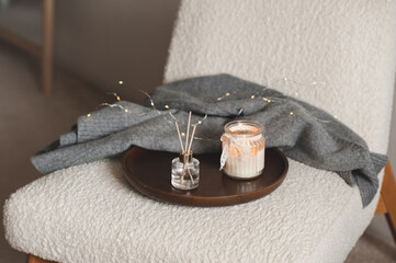 Cozy home atmosphere with liquid fragrance in glass bottle and burning scented candle with knit...