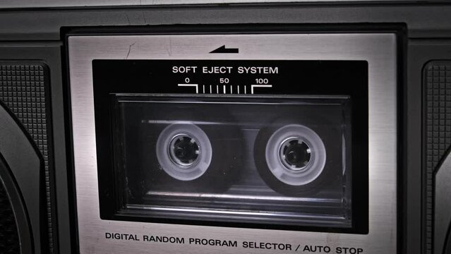 Audiocassette rotates in deck of old tape recorder. Transparent audio cassette in retro player spinning and playing. Close-up. Retro call recording, playback, reel playing, vintage technology 80s, 90s