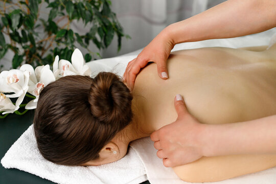 Female masseur massaging back and shoulder of young woman lying on massage table on white and green background.