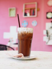 Ice coffee in a tall glass with cream poured over and coffee beans.