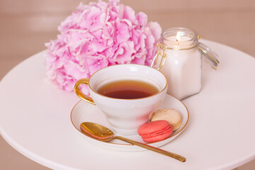 Cup of tea, macaroons, golden knife and fork and pink hydrangea flower on white table