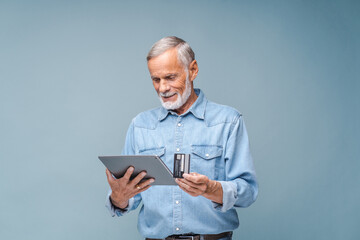 Elderly man writes payment details of credit card on website to make purchase via tablet. Focused...