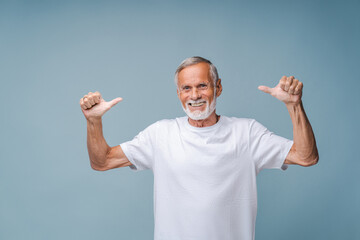 Happy senior man in white t-shirt shows thumbs-up gesture with hands smiling. Portrait of positive...