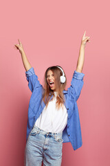 Cheerful young pretty woman listening music in headphones dancing over pink background. Closed eyes.