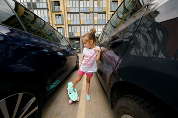 A child with a skateboard stands between two cars in a city parking lot. The danger of...