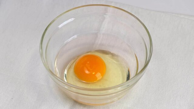 Breaking an egg into a glass bowl. Fresh organic egg falling into bowl. Close up.