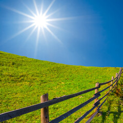Fototapeta premium green hill with wooden fence at summer sunny day, countryside rural landscape