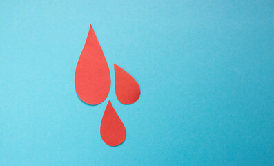 The concept of the World Blood Donor and Hemophilia Day. Red paper drops of blood on a blue...