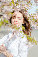 Obraz na płótnie Canvas Girl in a white shirt near the sakura trees. Sakura blossoms. Spring.