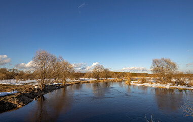 March sunny day by the river. A picturesque landscape, early spring, a river with snow-covered banks. The first thaws, the snow is melting.