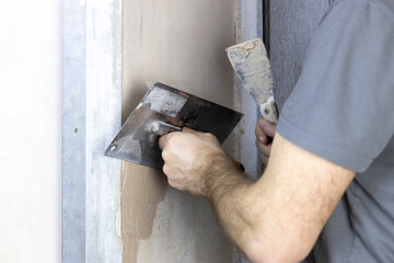 A worker applies plaster to a wall with a spatula.