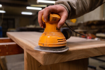 Closeup of carpenter sanding wood table with orbital sander in a workshop