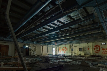 inside an old industrial military base hall with broken electric switch cabinets and pipes at the ceiling