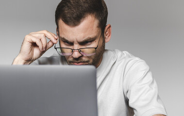 Adult man wearing glasses staring at screen of his laptop. - obrazy, fototapety, plakaty