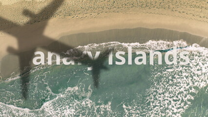 Shadow of a flying airliner reveals Canary Islands text on the sandy beach