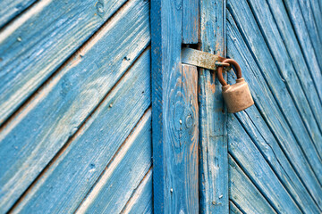 Old padlock on a weathered retro blue wooden door. Textured background.