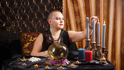 A bald woman fortuneteller lights black candles in a magic salon.